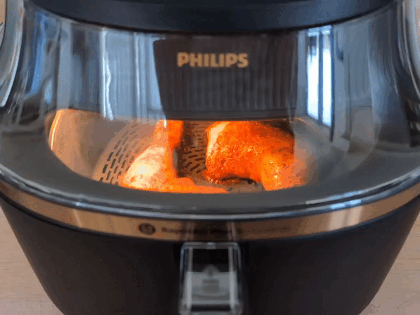 Zoom ins Innere des Philips Airfryer 3000 Series NA332/00, in dem zwei Hähnchenschenkel brutzeln.