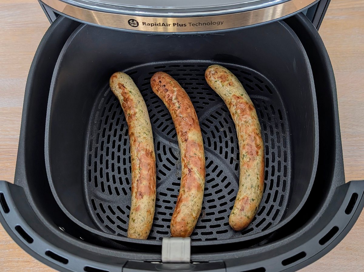 Blick von oben auf drei Würstchen, die im Innenkorb des Philips Airfryer 3000 Series 6,2 l ungleichmäßig garen.