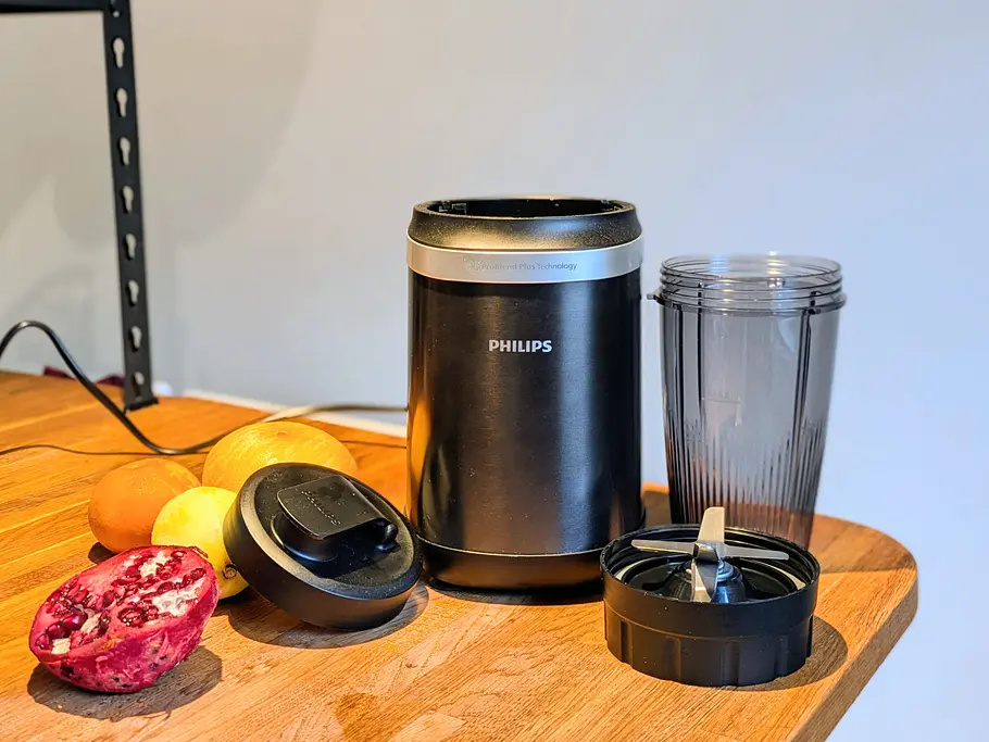 Der Philips 5000 Series Smoothiemaker steht auf der Holzplatte, Mixbehälter und Zubehör liegen daneben, Obst ist im Hintergrund.