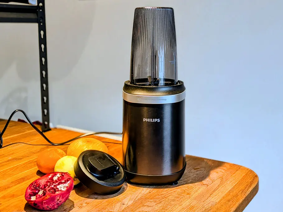 Der Philips 5000 Series Smoothiemaker steht auf einer Holzplatte, daneben liegen Obst und der abgenommene Deckel.