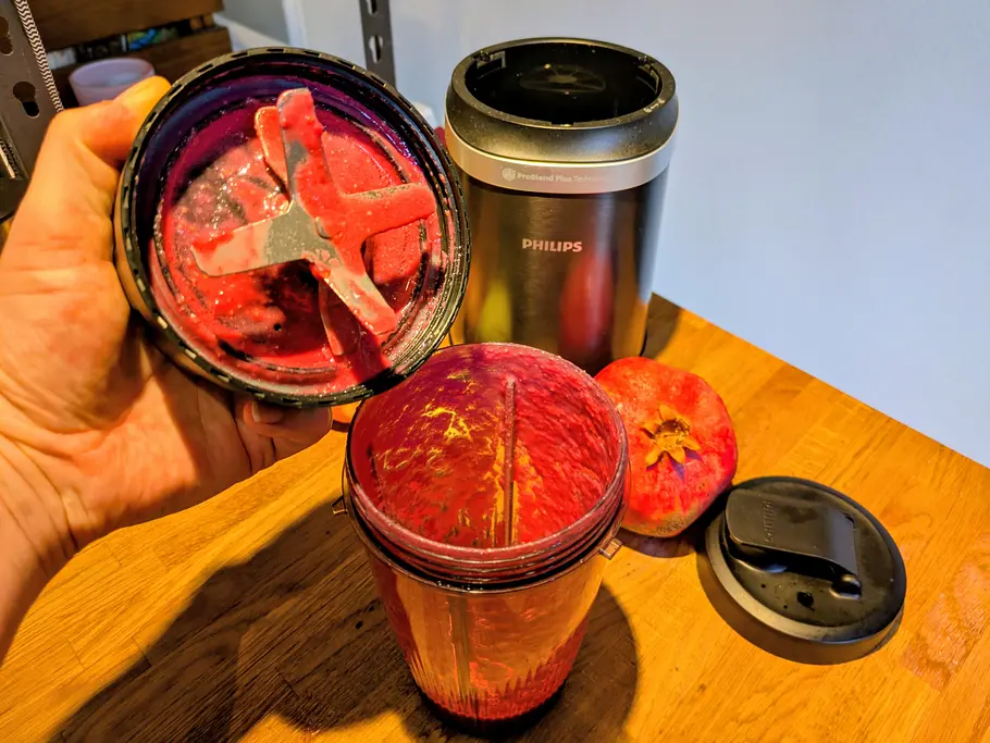 Eine Hand hält das Mixmesser des Philips 5000 Series Smoothiemaker, der gefüllte Behälter und Obst liegen auf der Arbeitsplatte.