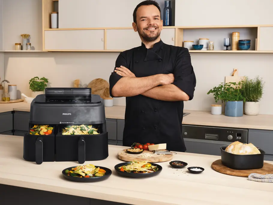 Der neue Philips-Airfryer Dual Basket von Steffen Henssler Vor einer modernen Küche präsentiert Profi-Koch Steffen Henssler den neuen Philips-Airfryer Dual Basket mit beiden aufgezogenen Schubladen und diversen zubereiteten Speisen aus der Heißluftftritteuse