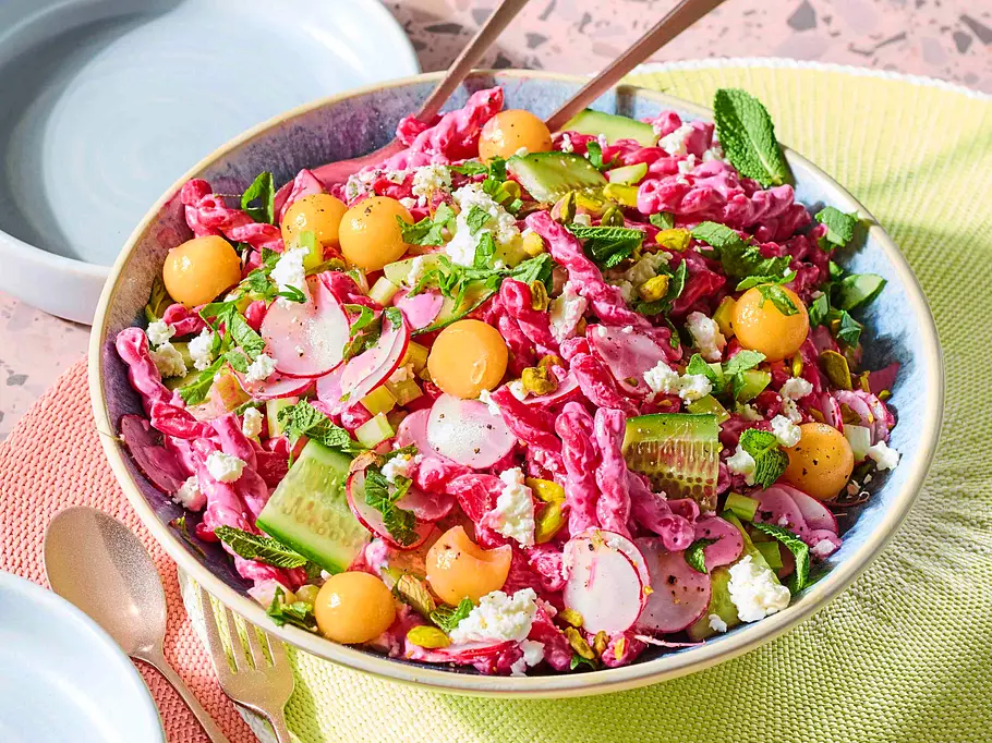 Pinker Nudelsalat mit fruchtigen Melonen-Bällchen Rezept Rosaroter Nudelsalat mit fruchtigen Melonen-Bällchen und Gurke und Radieschen in einer Schüssel angerichtet.