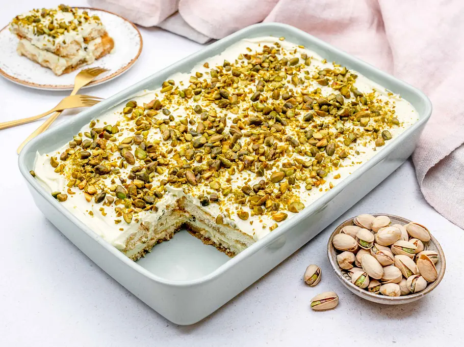 Pistazien-Tiramisu Rezept Eine rechteckige Auflaufform ist mit hellem Tiramisu gefüllt und großzügig mit gehackten Pistazien bedeckt.