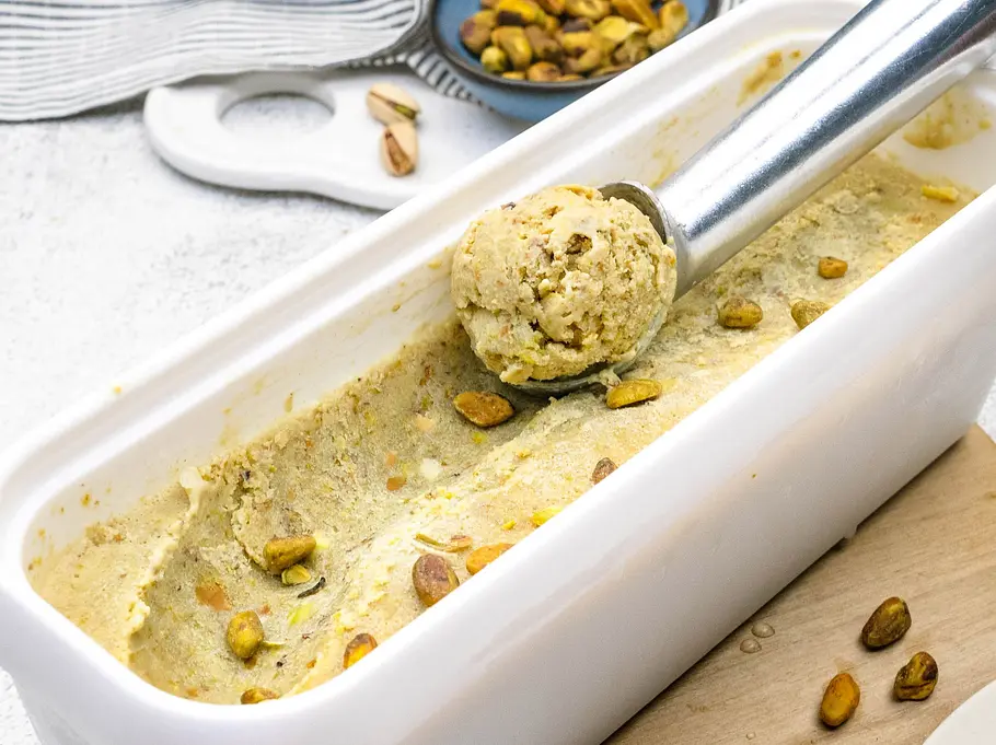 Pistazieneis Rezept Eine Eisform halb gefüllt mit Pistazieneis. Ein Portionierer formt darin eine Eiskugel.