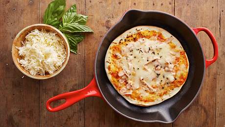 Eine Pizza in einer Pizzapfanne neben einer Schüssel Parmesan - Foto: iStock/martiapunts