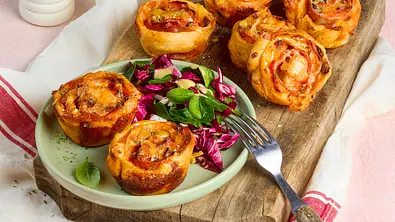Goldbraune Teigschnecken liegen auf einem Holzbrett und einem grünen Teller mit Blattsalat. Dahinter stehen Salat und ein Glas. - Foto: StockFood Studios / Meike Bergmann Goldbraune Teigschnecken liegen auf einem Holzbrett und einem grünen Teller mit Blattsalat. Dahinter stehen Salat und ein Glas. - Foto: StockFood Studios / Meike Bergmann