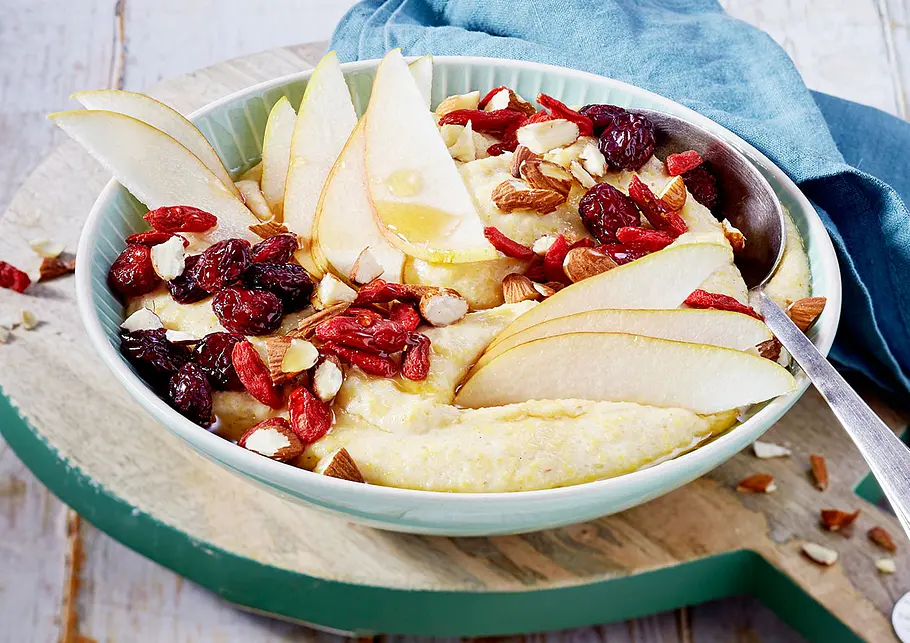 Eine flache Schüssel mit Polenta, Birnenspalten, Rosinen und Goji-Beeren.