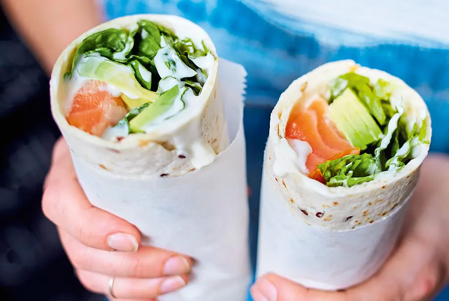 Tortilla-Wraps mit Lachs und Avocado Frauenhände halten zwei Power Wraps mit Lachs, Avocado und Römersalat