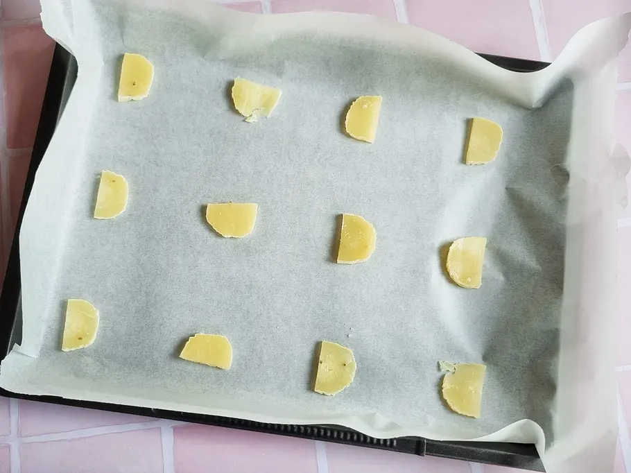 Harzer Käse-Stücke liegen mit Abstand auf ein mit Backpapier ausgelegtem Backblech.