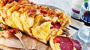Angeschnittenes Pizza-Zupfbrot mit einer sichtbaren Salami-Füllung liegt auf einem Holzbrettchen - Foto: House of Food / Bauer Food Experts KG