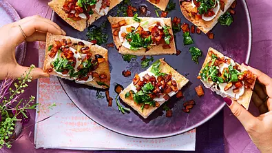 Kürbis-Bruschetta mit Ziegenkäse auf einem lila Teller, von dem sich zwei Hände zwei Stücke nehmen. - Foto: LECKER @ Bauer Media Group Kürbis-Bruschetta mit Ziegenkäse auf einem lila Teller, von dem sich zwei Hände zwei Stücke nehmen. - Foto: LECKER @ Bauer Media Group