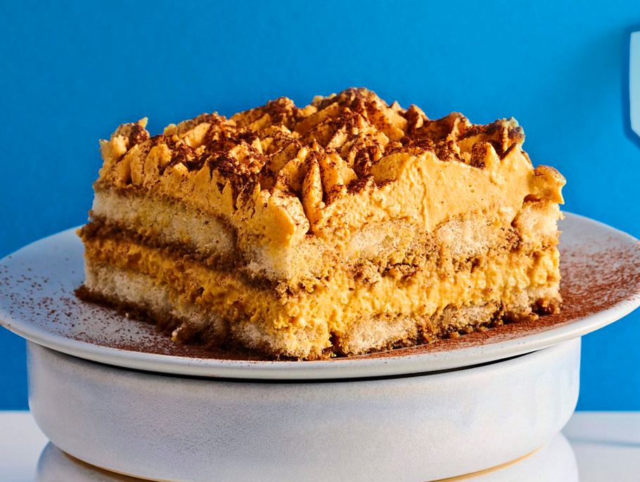 Ein großes rechteckickes Tiramisustück mit goldgelber Kürbis-Mascarpone und Kakao als Garnitur.