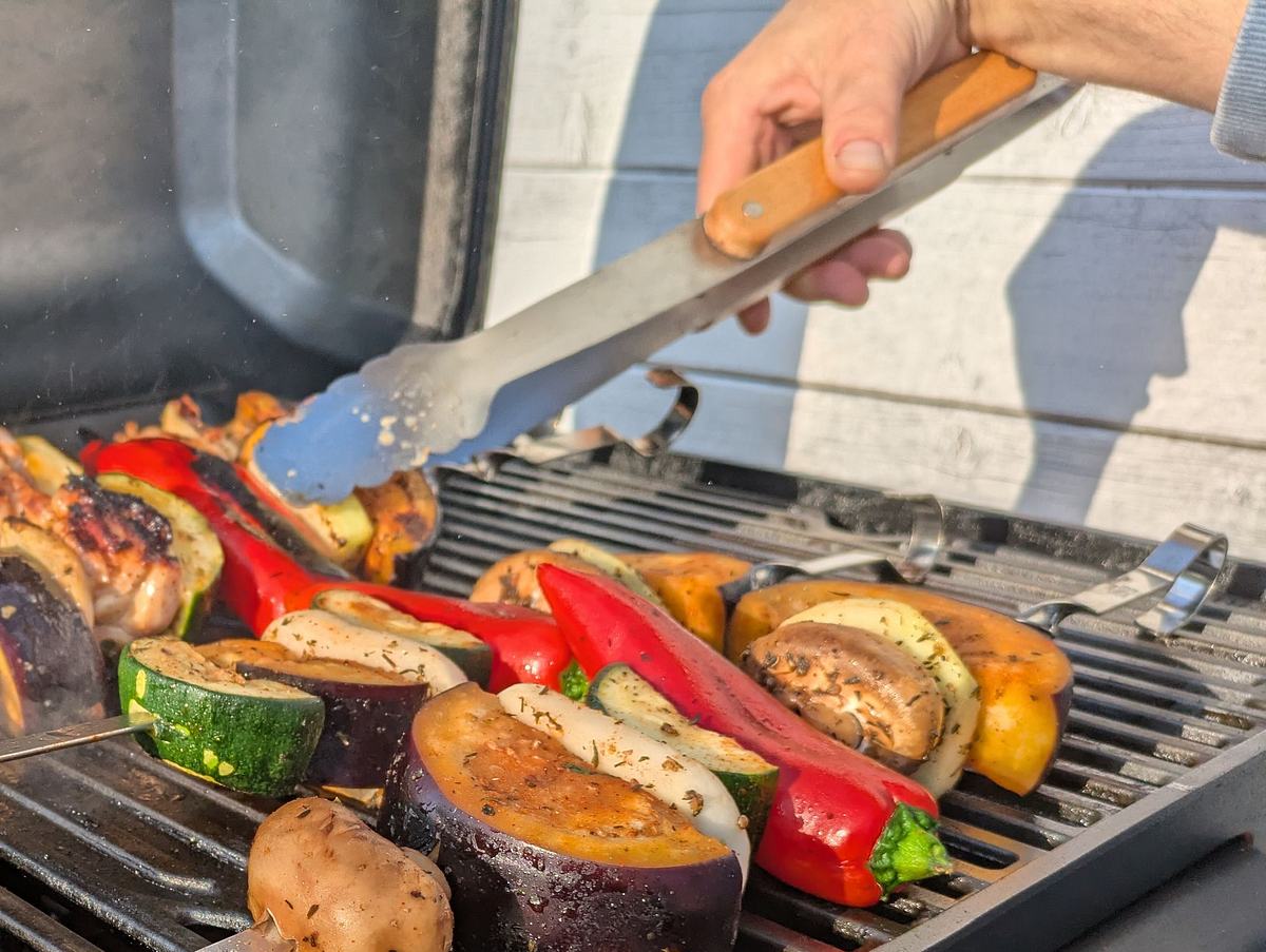 Grillspieße werden mithilfe einer Grillzange gewendet.