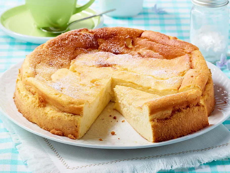 Quarkkuchen ohne Boden, ist angeschnitten und mit wenig Puderzucker bestäubt.