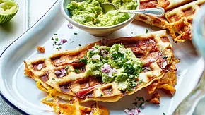 Knusprig gebackene Quesadillas mit geschmolzenem Käse und Speck, serviert mit Guacamole und gehackten roten Zwiebeln auf einem Teller. - Foto: LECKER @ Bauer Media Group Knusprig gebackene Quesadillas mit geschmolzenem Käse und Speck, serviert mit Guacamole und gehackten roten Zwiebeln auf einem Teller. - Foto: LECKER @ Bauer Media Group