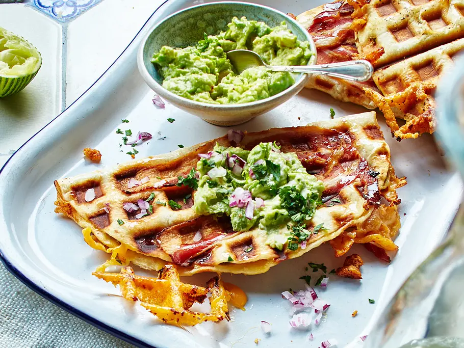  Knusprig gebackene Quesadillas mit geschmolzenem Käse und Speck, serviert mit Guacamole und gehackten roten Zwiebeln auf einem Teller.