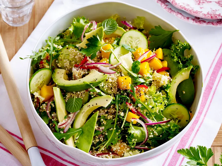 Quinoa-Salat mit Mango und Avocado Eine große Salatschüssel mit Quinoa tri colore, Avocadospalten, Gurkenscheiben, Mangowürfeln und Kräutern.