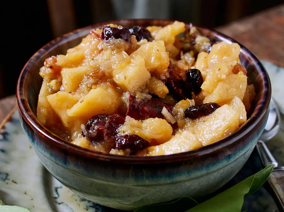 Süß-säuerliches Quitten-Chutney mit Fruchtstücken und Trockenfrüchten, serviert in einer kleinen rustikalen Schale auf einem marmorierten Unterteller.