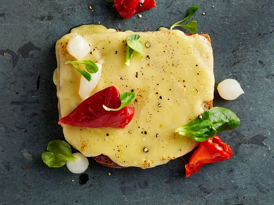 Raclette-Brot Rezept Raclette-Brot mit zerlaufenem Raclette-Käse, garniert mit Silberzwiebeln und eingelegter Paprika.