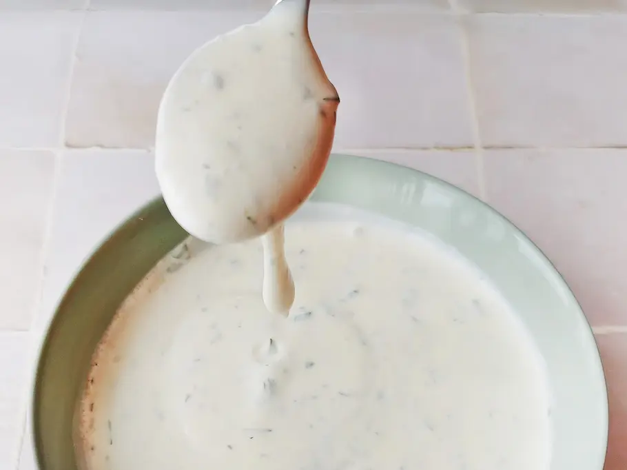 Ranch-Dressing läuft cremig von einem Löffel Cremiges Ranch-Dressing läuft von einem Teelöffel in die darunter stehende Schale mit Dressing