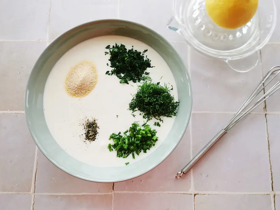 Ranch-Dressing-Basis in einer Schale, on top drei Häufchen gehackte Kräuter, schwarzer Pfeffer und Zwiebelpulver