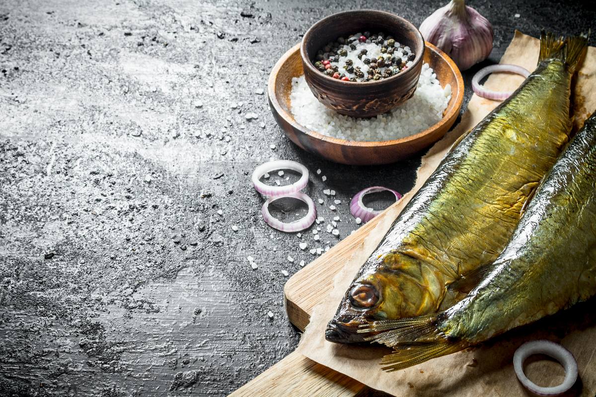 Geräucherter Fisch auf einem Holzbrett, garniert mit Zwiebeln und Pfeffer