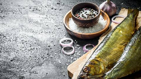 Geräucherter Fisch auf einem Holzbrett, garniert mit Zwiebeln und Pfeffer - Foto: iStock/Olesia Shadrina