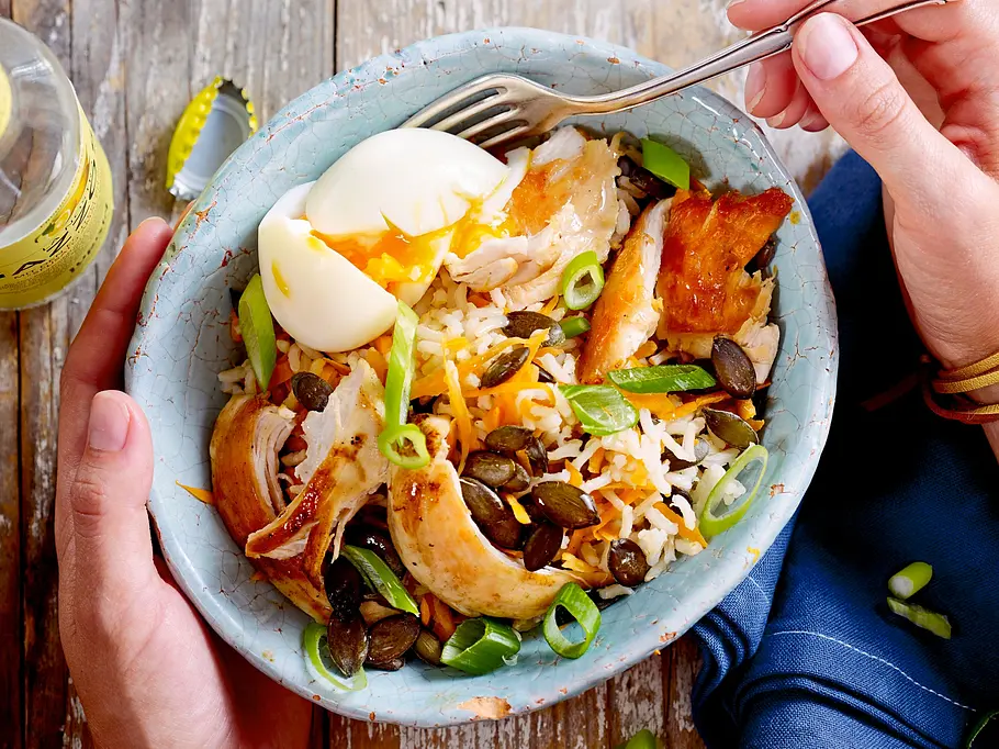 Reis-Bowl mit Hähnchen und Ei Rezept Eine blaue Reis-Bowl mit Hähnchen und Ei und Frühlingszwiebeln. Zwei Hände halten eine Gabel.