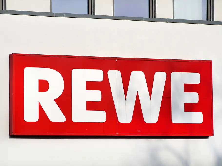 REWE-Schild an einer weißen Häuserwand REWE-Schild an einer weißen Häuserwand