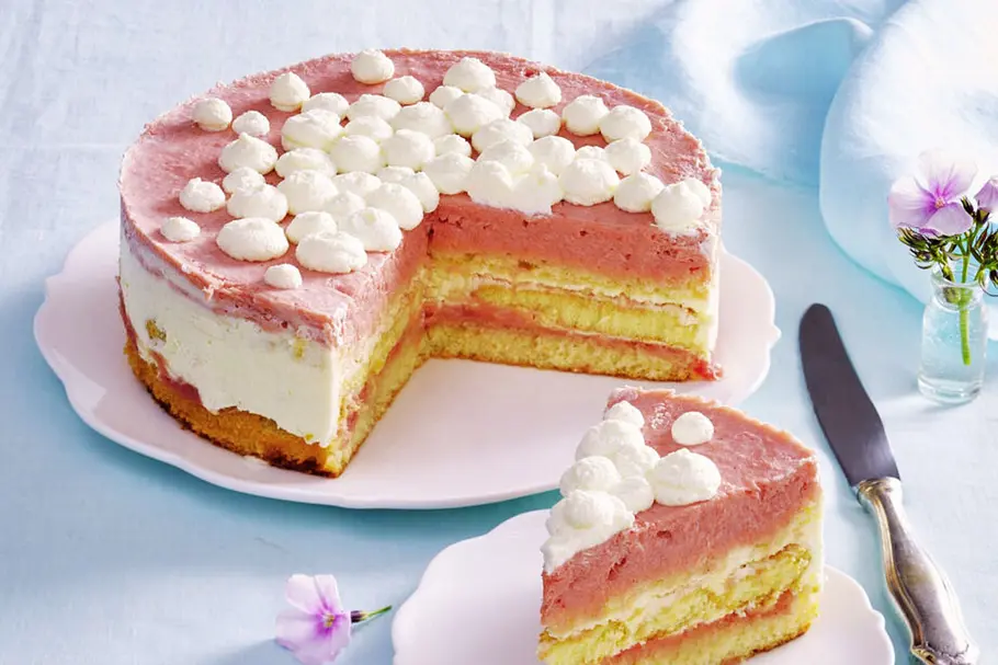 Rhabarber-Frischkäse-Torte Eine Rhabarber-Frischkäse-Torte angeschnitten auf einem weißen Teller. Rechts daneben ein Kuchenstück ebenfalls auf einem weißen Teller.