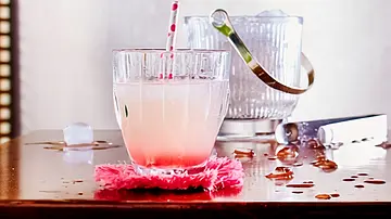 Ein Glas Rhabarber-Limonade mit Papierstrohhalm auf einem pinken Stoff-Untersetzer im Hintergrund ein Eiswürfelbehälter aus Glas. - Foto: LECKER @ Bauer Media Group Ein Glas Rhabarber-Limonade mit Papierstrohhalm auf einem pinken Stoff-Untersetzer im Hintergrund ein Eiswürfelbehälter aus Glas. - Foto: LECKER @ Bauer Media Group