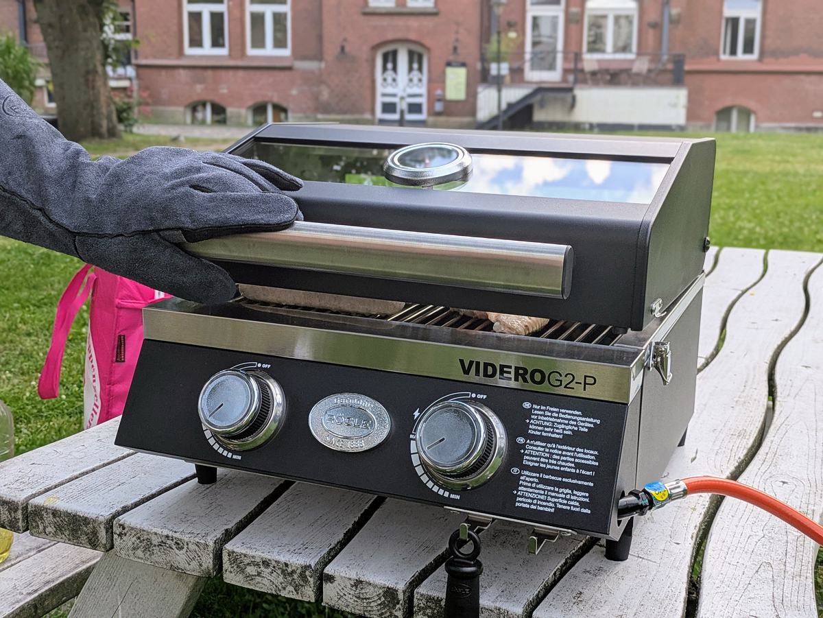 Hand mit Grillhandschu am Griff des Rösle Videro G2-P Campinggrills.