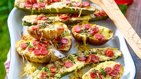 Gefüllte Zucchini und Kartoffeln mit geschmolzenem Käse, kleinen Salami-Scheiben und frischen Kräutern auf einem Tablett. - Foto: House of Food / Bauer Food Experts KG