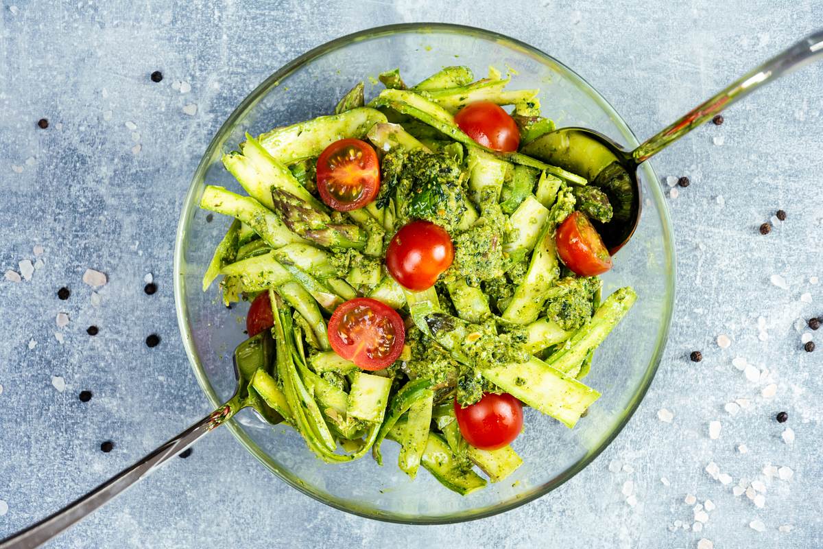 Pastasalat in einer Glasschüssel und Salatbesteck aus Edelstahl