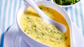 Eine Sauciere mit buttergelber Sauce béarnaise und frisch gehackten Kräutern steht mit einem Soßenlöffel auf einem Tisch mit blau-weiß gestreiftem Tischtuch - Foto: LECKER @ Bauer Media Group