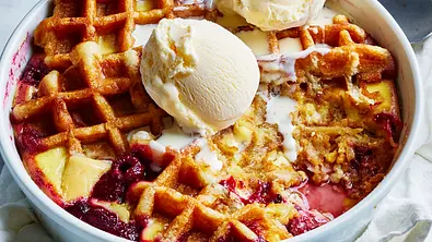 Waffel-Pudding-Auflauf mit Himbeeren in einer Auflaufform, serviert mit Vanilleeis und cremiger Soße. - Foto: Image Professionals