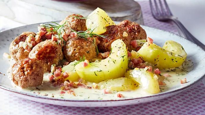 Die Schmorgurken liegen in cremiger Soße auf einem hellen Teller im Vordergrund. Dahinter sind Hackbällchen zu sehen. - Foto: LECKER @ Bauer Media Group Die Schmorgurken liegen in cremiger Soße auf einem hellen Teller im Vordergrund. Dahinter sind Hackbällchen zu sehen. - Foto: LECKER @ Bauer Media Group
