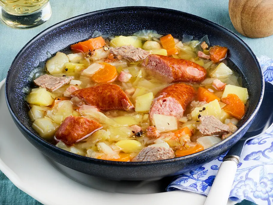 Eine Schale ist gefüllt mit würzigem Eintopf aus Steckrübe, Möhren, Suppenfleisch und geschnittener Schmorrwurst.