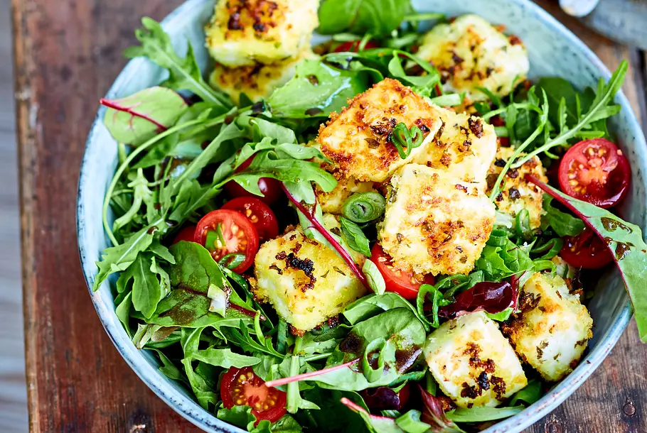 Knusper-Feta aus dem Airfryer Auf einer großen Schüssel Salat befinden sich knusprige Fetawürfel.
