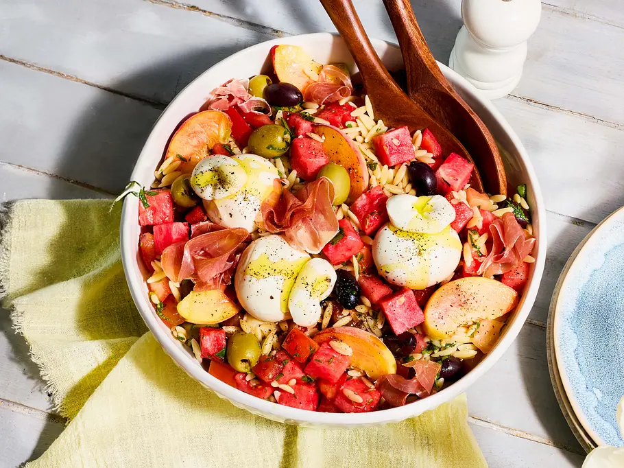 Schneller Kritharaki-Salat mit Wassermelone, Burrata und Pfirsichen Eine große Schüssel mit Kritharaki-Salat mit Wassermelone, Burrata, Pfirsichen und schwarzen und grünen Olien.