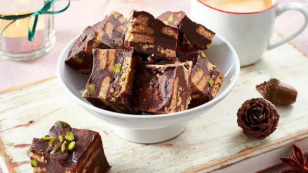 Schoko-Konfektwürfel mit Keksen und Pistazien in einer weißen Schale auf einem Holzbrett, dazu eine Tasse Kaffee. - Foto: LECKER @ Bauer Media Group