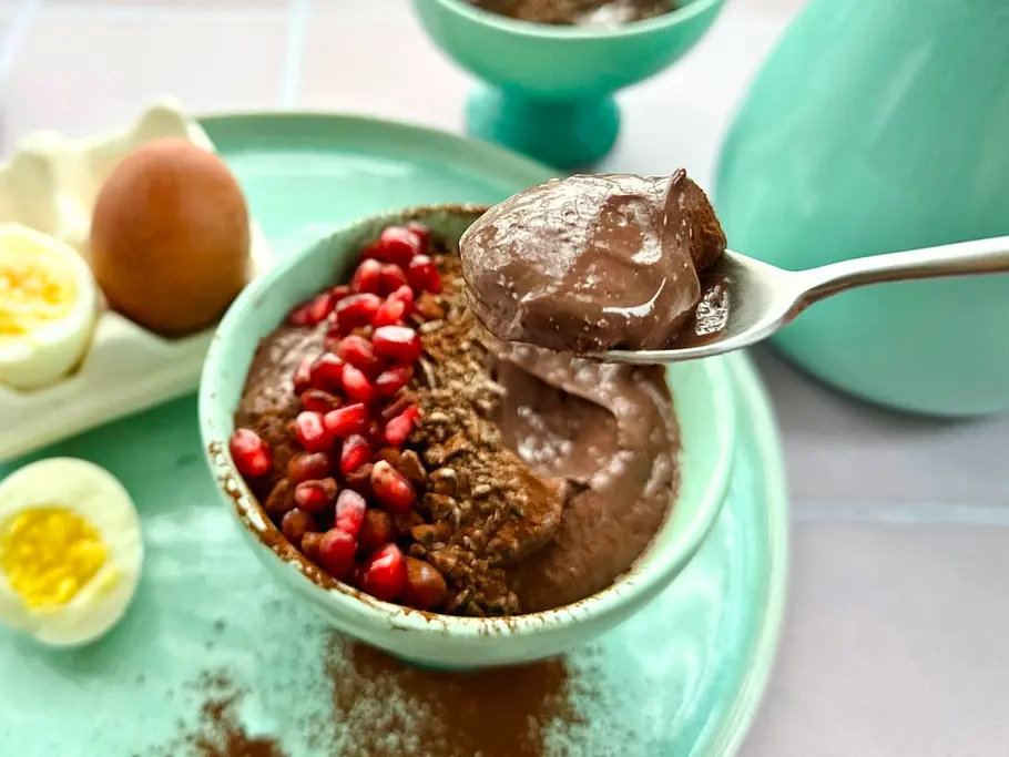 Schokopudding mit vielen Proteinen aus gekochten Eiern Eine Schale mit angelöffeltem Protein-Schokopudding mit einem Granatapfel-Topping und ein Löffel voll cremigem Pudding