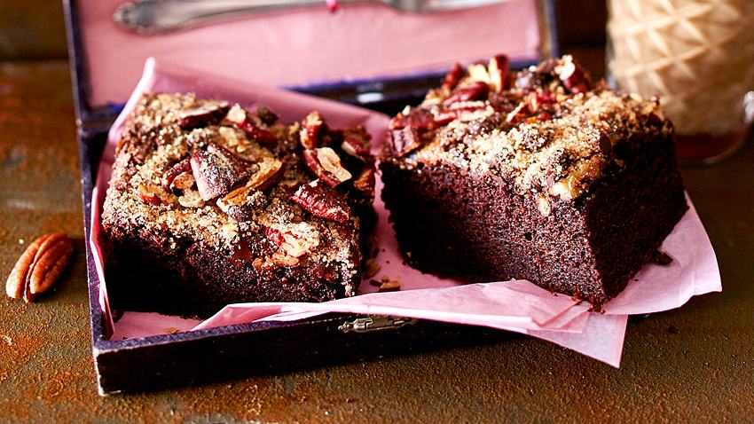 Zwei quadratische Stücke Schoko-Zucchini-Kuchen mit Pekannuss-Topping auf einer rosa Serviette. - Foto: House of Food / Bauer Food Experts KG