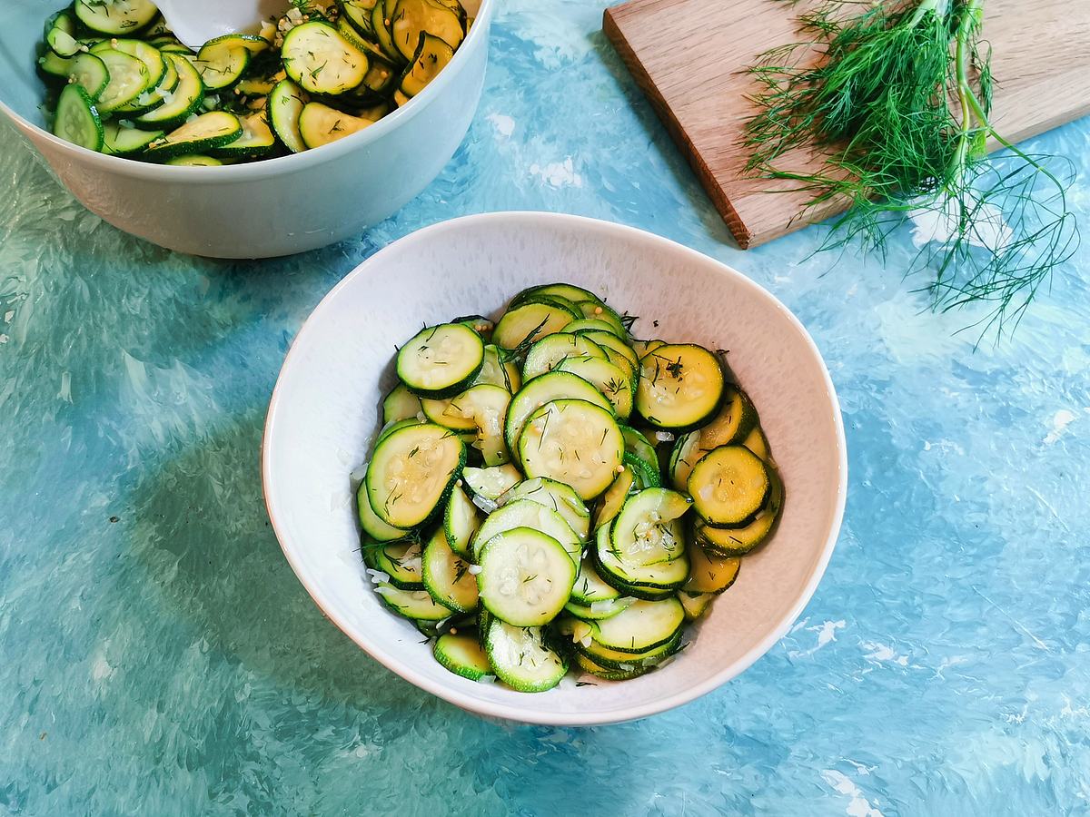 In dünne Scheiben geschnittene Zucchini in einer Schale als Salat serviert, im Hintergrund ein Bund frischer Dill