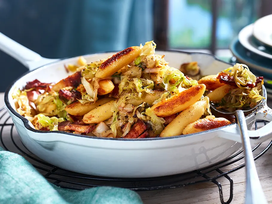 Eine weiße Pfanne mit Schupfnudeln, Spitzkohl und Speck, man sieht deutliche Röstspuren