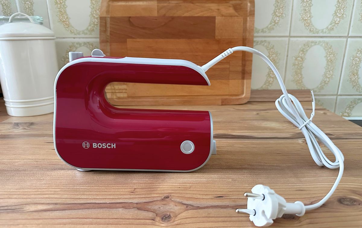 Der Bosch-Handmixer steht seitlich auf der Arbeitsfläche. Dabei ist die hübsche magentar-rote Seite und der grau beschichte Griff sichtbar