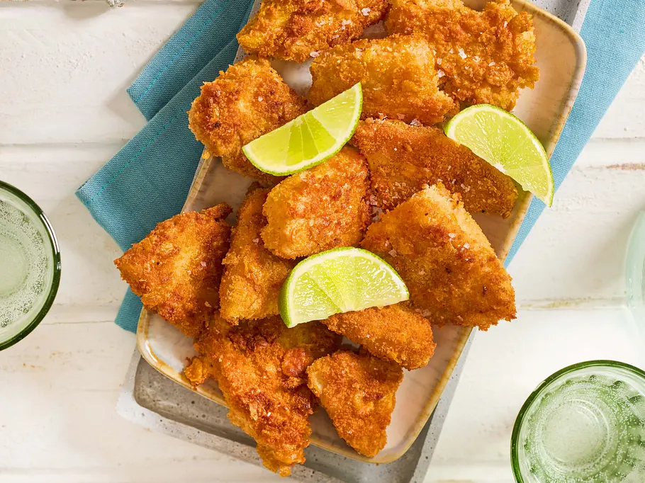 Goldbraune Sellerie-Nuggets mit Limettenspalten auf einem Teller serviert.