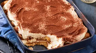 Skyr-Tiramisu in einer rechteckigen Auflaufform, mit Kakaopulver bestäubt, eine Portion ist bereits herausgenommen; serviert auf einem Tisch. - Foto: LECKER @ Bauer Media Group 
