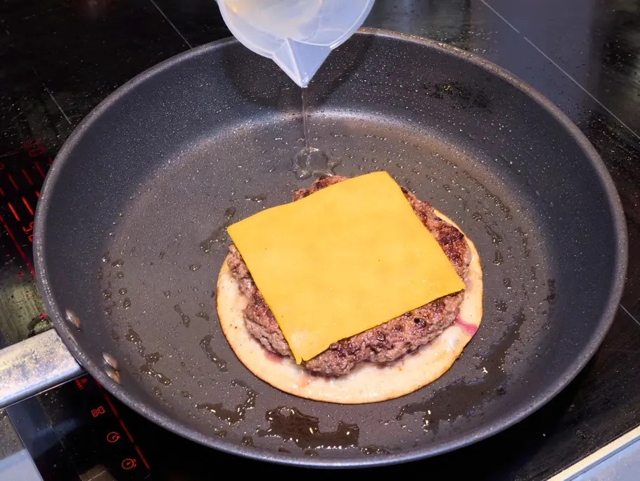 Smashed Cheeseburger-Tacos Rezept Ein Taco belegt mit Hackfleisch und einer Scheibe Ceddar wird in einer Pfanne gebraten.